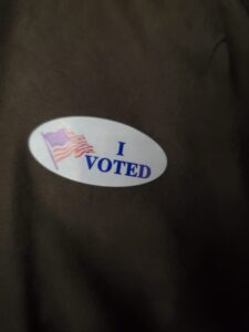 Oval sticker with American flag and the words I Voted in blue